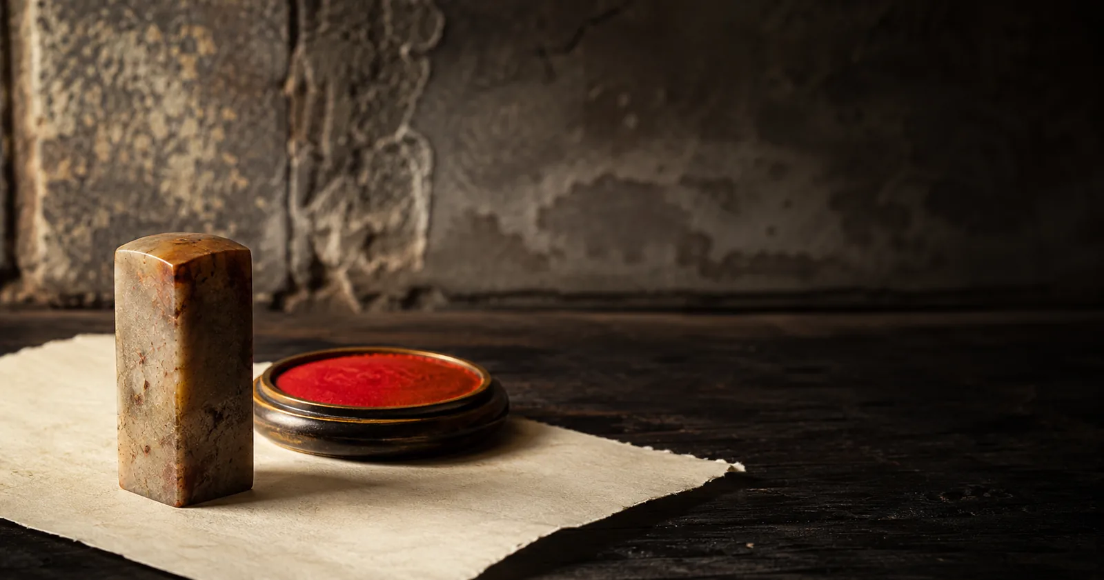 A carved stone seal standing on handmade paper beside an open dish of red seal paste.